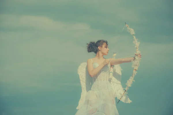 Meisje in witte engelen jurk, cupido met vleugels richten met pijl en boog op een hemel achtergrond. Valentijnsdag concept. Engel tiener in de hemel. — Stockfoto