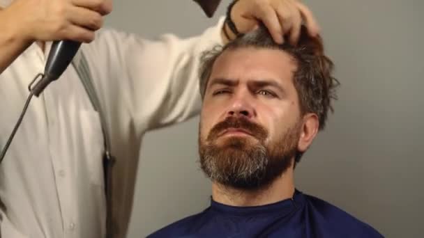 Barbiere. Parrucchiere professionista con asciugacapelli pettinano capelli di uomo in negozio di barbiere. Barbiere fare taglio di capelli a uomo attraente in barbiere. — Video Stock