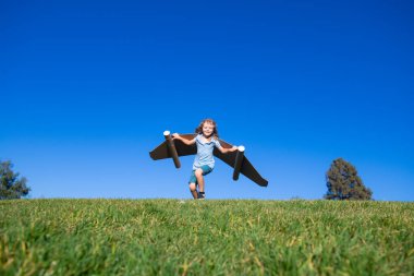 Mutlu çocuk dışarıda yeşil çimlerde ve mavi gökyüzünde oynuyor. Oyuncak jetpack 'li çocuk pilot. Çocuk oyuncak uçak kartonuyla oynuyor. Yaz seyahati ve macera. Başarı, hayal gücü ve rüya konsepti.