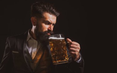 Klasik takım elbiseli adam bira içiyor. Sakallı adam siyah arka planda yüksek bardakta bira kaldırmaktan memnun..
