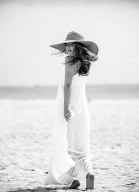 Plajda poz veren yaz modeli. Yazlık kadın kıyafetleri. Hasır şapkalı, yazlık elbiseli, yaz trendi tarzında genç ve güzel bir hippi kadın..