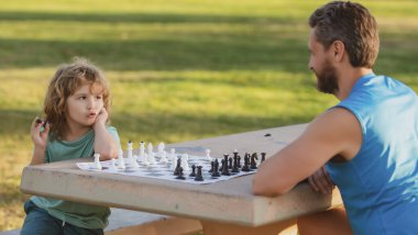 Baba ve oğul parkta birlikte satranç oynuyorlar. Çocuklar için oyunlar ve etkinlikler.