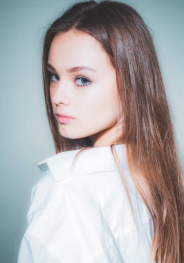 Güzel yüzlü, kameraya bakan, beyaz gömlekli, uzun saçlı, neşeli, güzel bir kızın portresini yakından çek. Gri arkaplandan kameraya bakan güzel, sevimli, neşeli bir kız..