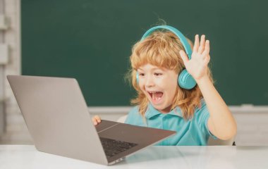 Heyecanlı çocuklar için duygular. Kulaklıklı çocuk dizüstü bilgisayar kullanıyor ve okuldaki video öğretmeniyle internetten çalışıyor..