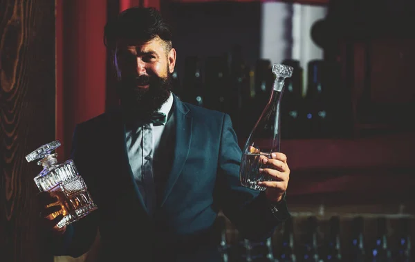 Przystojny brodaty barman z długą brodą i wąsami z poważną twarzą wykonany koktajl alkoholowy w starym garniturze na tle baru. — Zdjęcie stockowe