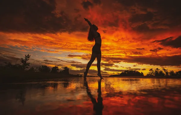 Silhouette nera di bella ragazza o bella donna, sexy modello sottile, con i capelli lunghi posa sulla spiaggia al tramonto all'aperto su sfondo cielo viola — Foto Stock