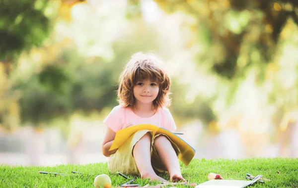 Fernstudium. Nettes lächelndes amerikanisches Kind lernt und schreibt mit Bleistift im Freien im Park. — Stockfoto