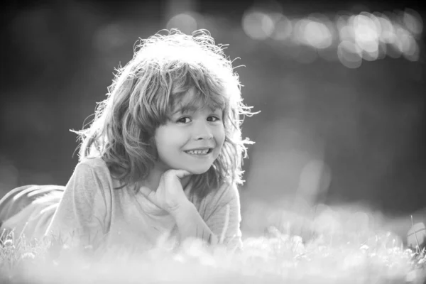 Portret van een vrolijk lachend kind liggend op gras in het zomerse natuurpark. close-up positieve kinderen gezicht. — Stockfoto