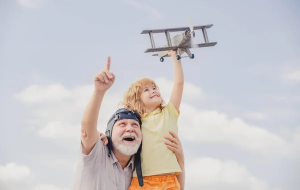 Jovem neto e velho avô brincando com avião de brinquedo contra o fundo do céu de verão. — Fotografia de Stock