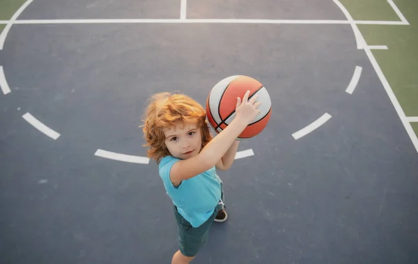 Roztomilý chlapeček držící basketbalový míček se snaží skórovat. Sport pro děti, pohled shora. — Stock fotografie