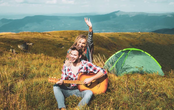 Feliz pareja de amigos acampando, y tocando la guitarra juntos en verano en el bosque natural. Pareja enamorada en el campamento . — Foto de Stock