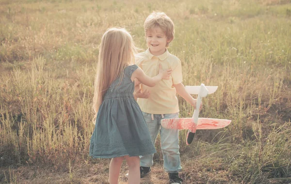 Une histoire d'amour. Deux enfants heureux garçon et fille jouant avec jouet avion sur prairie avoir du plaisir et sourire. Enfants heureux - sœur et frère sur le champ d'été. Aventure et vacances concept enfants . — Photo