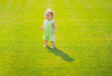 Yeşil çimlerin üzerinde çıplak ayakla duran bebek. Küçük çocuk yaz parkında oynuyor. Mutlu çocukluk ve çocuk sağlığı hizmetleri.