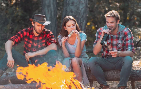 Friends relaxing near campfire after day hiking or gathering mushrooms. Tourism concept. Best friends spend leisure weekend hike barbecue forest nature background.