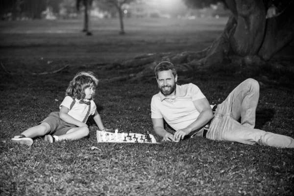 Sohn liegt auf Gras und spielt Schach mit Vater. Junge schlägt Mann beim Schach. — Stockfoto
