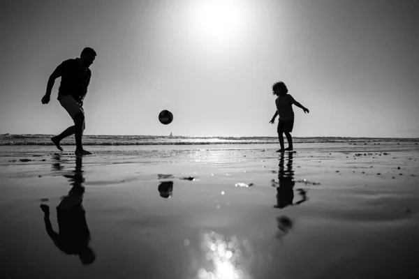 夏の日に遊んでいる子供の男の子とお父さん。父と息子は夏休みにビーチでサッカーやサッカーをする. — ストック写真