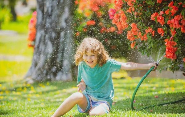 Mutlu çocuk hortumdan su döküyor. Bahçede çiçekleri sulayan çocuk. Evde bahçe işleri..