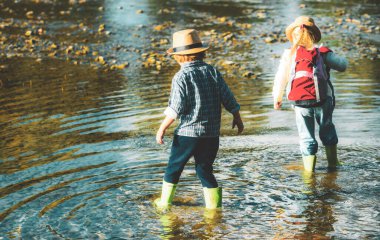 Nehirde sırt çantalarıyla yürüyüş yapan iki çocuk. Derede oynayan tatlı sarışın kız ve oğlan. Çocuklar orman deresinde yürüyor ve doğayı keşfediyorlar. Yaz çocukları eğlencesi. Çocuklar yaz aktiviteleri.