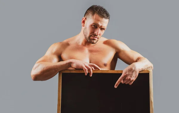 Hombre de fitness con cartel publicitario. Guapo musculoso culturista sosteniendo cartel en blanco aislado sobre fondo gris. —  Fotos de Stock
