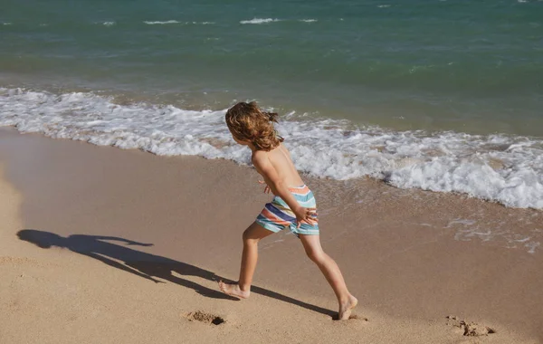 Happy kid boy amusez-vous sur la plage de la mer tropicale. Enfant drôle courir avec des éclaboussures par la piscine d'eau le long du bord de surf. Activité pour enfants pendant les vacances d'été. — Photo