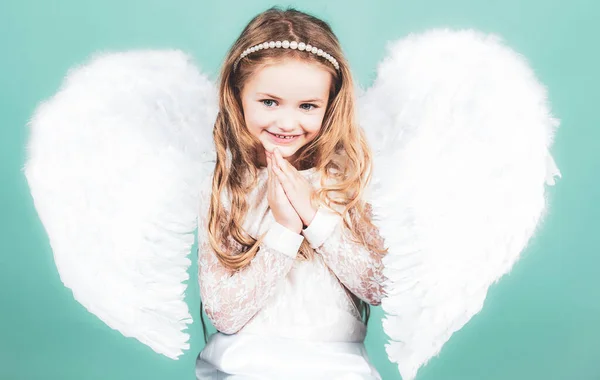 Piękna mała anielska dziewczynka stojąca z rękoma blisko klatki piersiowej jak w modlitwie. Aniołki trzymają się za ciebie z daleka. Złośliwa mała aniołek dziewczyna stojąca z zaciśniętymi pięściami. — Zdjęcie stockowe
