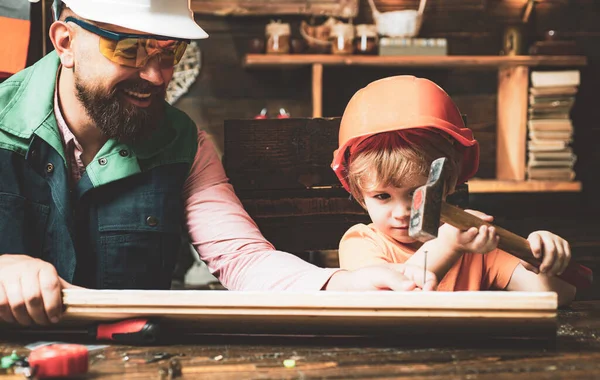 Vroege ontwikkeling. Vader en zoon als bouwer of reparateur. Vader en zoon met hamer en spijkers tegen een houten muur. Gelukkige vaders dag concept. Kweken van kinderen. — Stockfoto