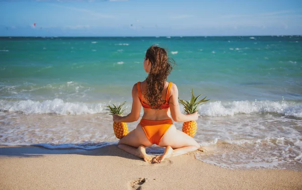 Sexy woman in swimsuits bikini hold pineapple near butt, buttocks on summer beach. — Stok fotoğraf