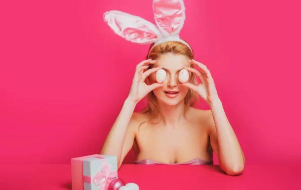 Una mujer encantadora disfrazada de conejo. Hermosa chica con orejas de conejo y huevos de Pascua sobre fondo rosa. — Foto de Stock