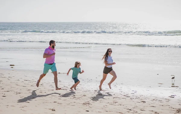 お父さん、お母さん、お子さんが海岸を走っています。健康的な家庭生活をコンセプトとする。夏休みの海で。健康的なライフスタイル. — ストック写真