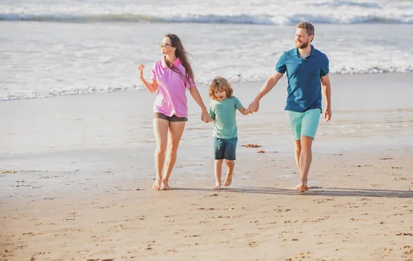 一家三口沿着海滨散步.父母牵着儿子的手在海滩上散步. — 图库照片