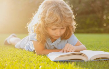 Dışarıda kitap okuyan sevimli bir çocuk. Çocuk parkta kitap okudu..