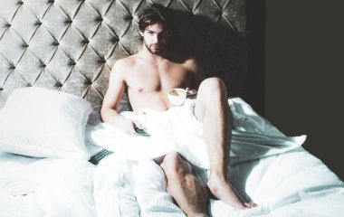 Üstsüz seksi erkek model yatak odasında tek başına yatıyor. Baştan çıkarıcı ve seksi adam..