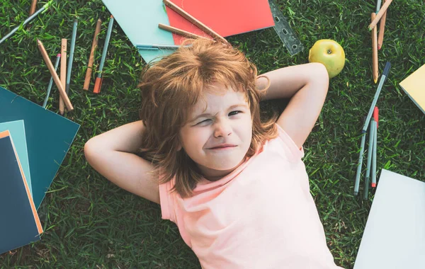 Kinder zwinkern. Kinder lernen und lernen draußen. Lustiger kleiner Schüler liest Buch im Freien, liegt auf dem Rasen im Park, lernt im Schulhof. — Stockfoto