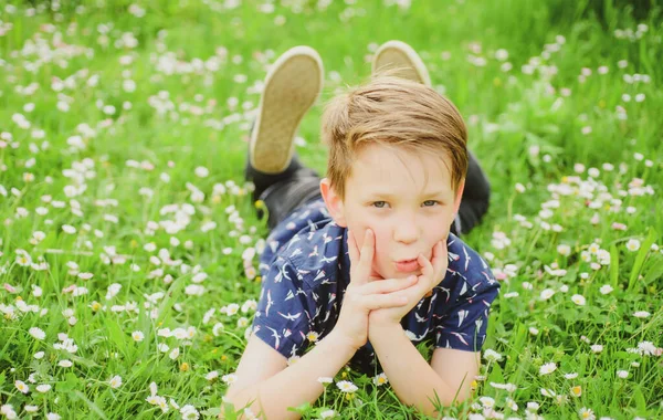 Vårpojken vilar på gräs. Söt unge på fältsblomma. Drömmande barn. — Stockfoto