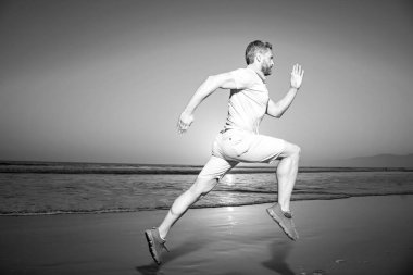 Koşan bir koşucu. Genç adam inanılmaz bir günbatımında denizin sahilinde koşuyor..