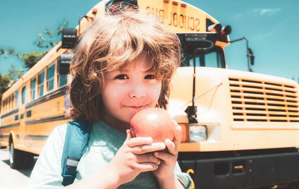 Schüler vor dem Schulbus beim Apfel essen. Kind aus Grundschule mit Tasche im Schulbus unterwegs. — Stockfoto