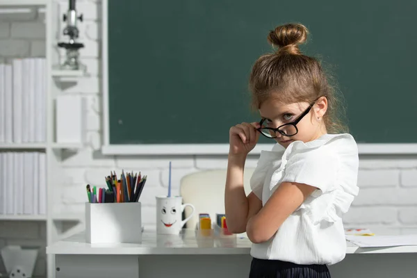 Kocka iskolás lány szemüvegben a táblán. Az általános iskolai tanulmányok vicces diáklányának portréja. — Stock Fotó