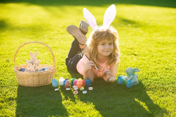 Дети празднуют Пасху. Мальчик в костюме кролика с кроличьими ушами, рисующий яйца на открытом воздухе. — стоковое фото