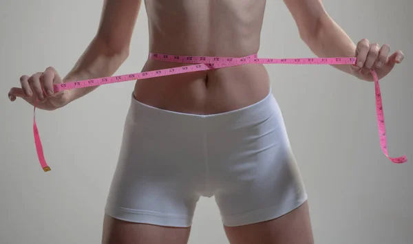 A medir a cintura. Feminino se encaixa corpo magro. Conceito de alimentação saudável e dieta. Menina com cintura perfeita com uma fita métrica. — Fotografia de Stock