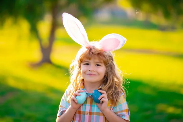 Cara de niño conejito. Niño cazando huevos de Pascua, poniendo en la hierba. Niño en conejo orejas de conejo al aire libre. Conejito de Pascua niños. —  Fotos de Stock