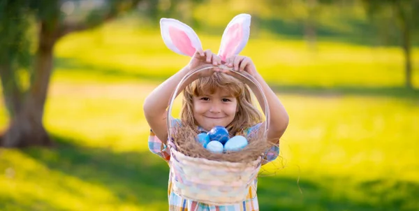 A kisfiú húsvéti tojásra vadászik. Gyerek fiú húsvéti tojással és nyuszifülekkel a parkban. Boldog Húsvétot!. — Stock Fotó
