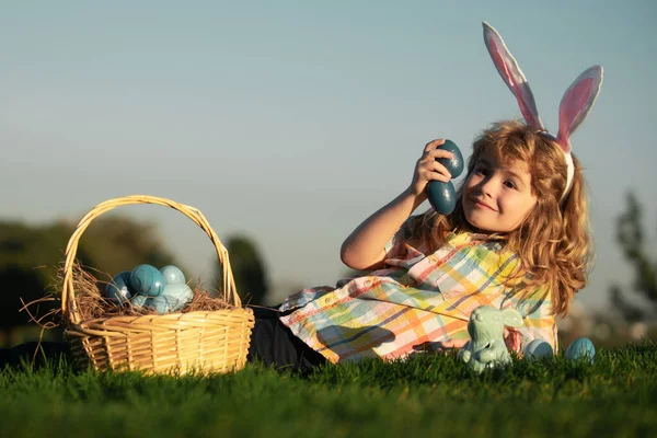 Chłopiec z wielkanocnymi jajkami w koszyku na świeżym powietrzu. Dzieciak leży na trawie w parku. Polowanie na pisanki. Twarz Fynny 'ego. Cute bunny dziecko chłopiec z króliczymi uszami na tle nieba z miejsca kopiowania. — Zdjęcie stockowe