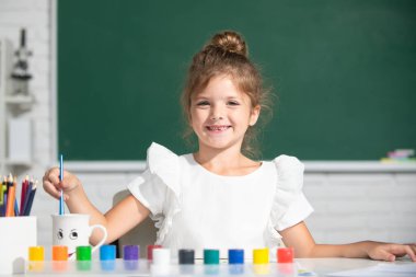 Boya rengi ve fırçayla resim yapan şirin bir kız çocuğu. Okulda resim dersi. Erken eğitim.
