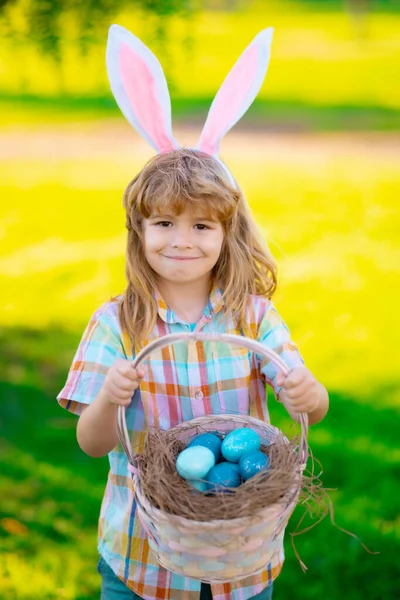 Veselé Velikonoce. Chlapec loví velikonoční vajíčka, snáší trávu. Dítě v králičích uších venku. Velikonoční zajíčci děti. — Stock fotografie