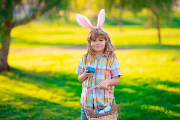 Feliz Pascua para los niños. Niño cazando huevos de Pascua, poniendo en la hierba. Niño en conejo orejas de conejo al aire libre. Conejito de Pascua niños. —  Fotos de Stock
