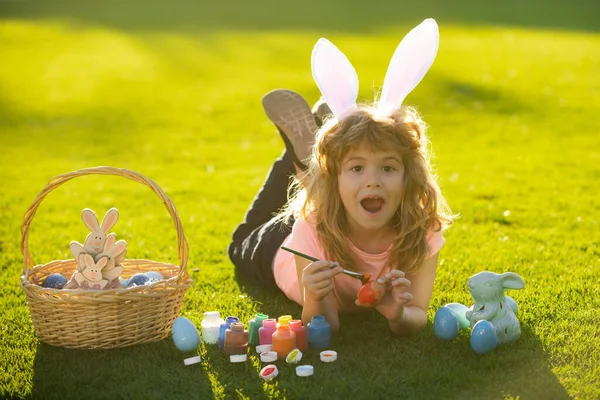 Chłopiec z wielkanocnymi jajkami i króliczymi uszami malujący jajka na zewnątrz. słodkie dziecko mając szczęśliwy Wielkanoc w park. — Zdjęcie stockowe