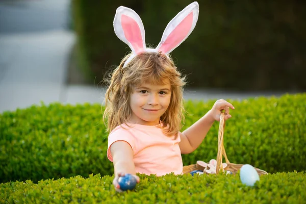 Niño cazando huevos de Pascua. Niño de Pascua en orejas de conejo cazando huevos de Pascua al aire libre. Lindo niño en traje de conejo con orejas de conejo divertirse en el parque. —  Fotos de Stock
