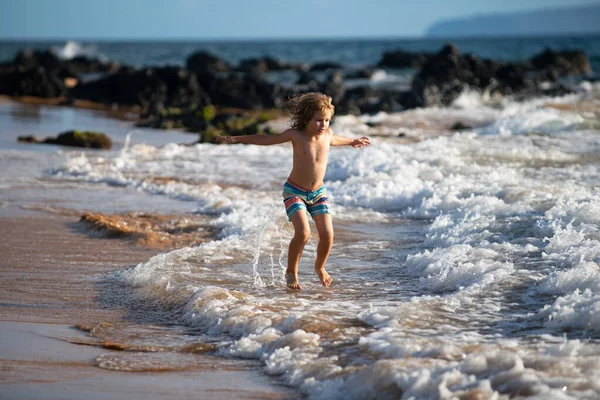 Kind spielt am Strand. Kind springt im Urlaub auf See in die Wellen. Kleiner Junge läuft während der Sommerferien am tropischen Strand einer exotischen Insel. — Stockfoto