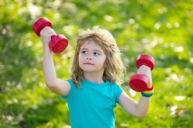 Dambıl kaldıran çocuk. Dambılı şirin çocuk eğitimi. Çocuk fitness. Çocuk dışarıda halterlerle egzersiz yapıyor. Komik heyecanlı çocuk sporcusu.