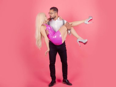 Yakışıklı, zarif genç bir adam kız arkadaşını kollarında tutuyor. Yaratıcı bebekler çift konsepti. Güçlü komik adam kollarında bir kadına sarılıyor..